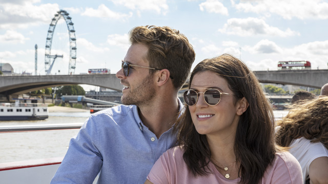 Un couple visite la ville de Londres utilisant le London Pass. Image fournie par Leisure Pass Group Un couple se tiennent côte à côte et se sourit lors d'une visite guidée de Londres avec le London Pass, tandis que l'on voit le London Eye à l'arrière plan.