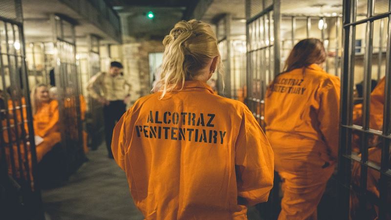 Prenez part à une expérience unique et en immersion complete avec Alcotraz Prison Cocktail Experience à Londres. Image fournie par Golden Tours. Une femme se présentant de dos et portant un uniforme de prison orange