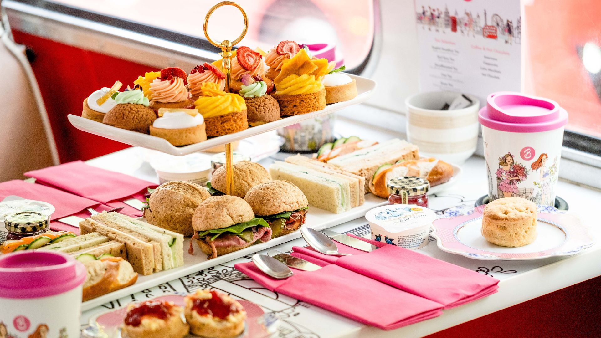 Tuck into sweet treats and savoury delights and spot famous London landmarks onboard Brigit's Bakery afternoon tea bus tour. Image courtesy of Brigit's Bakery. A table on a double decker bus covered in sandwiches and cakes with coffee cups.