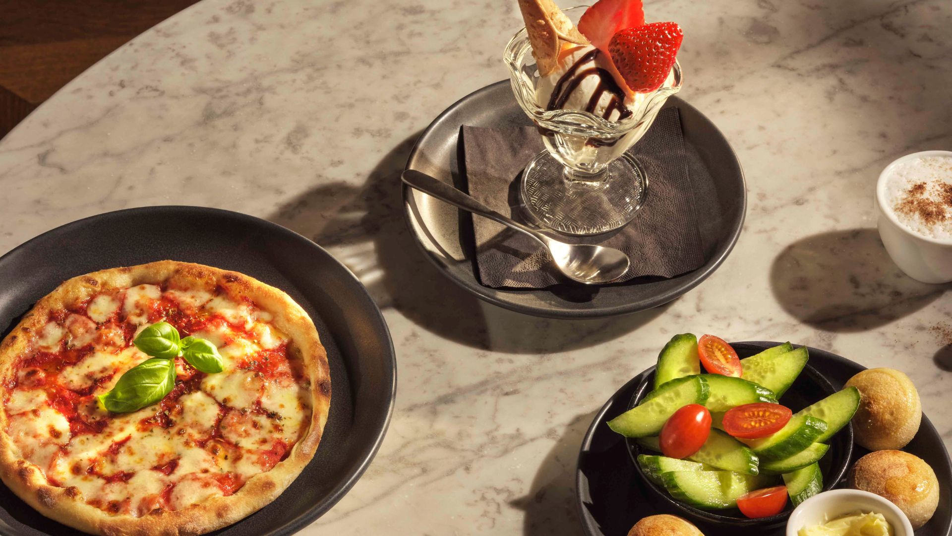 From mini pizzas to crunchy veggies and an indulgent sundae, the Piccolo children’s menu at PizzaExpress turns family dining into a fun and flavour-packed experience for younger guests. Image courtesy of Pizza Express. A children’s meal at PizzaExpress with a small pizza, cucumber and tomato salad, dough balls and an ice cream sundae on a table.