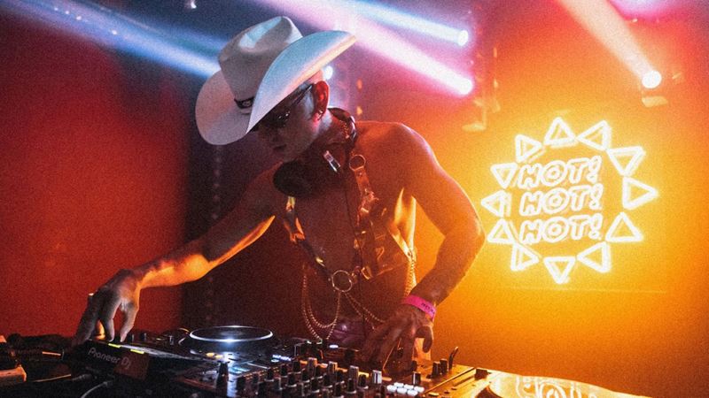 Book tickets to some of the most iconic gay club nights in the capital. Credit: House of Trash. Image courtesy of Electrowerkz. A photo of a DJ wearing a cowboy hat looking down onto DJ decks as he plays with a neon sign on the wall behind him
