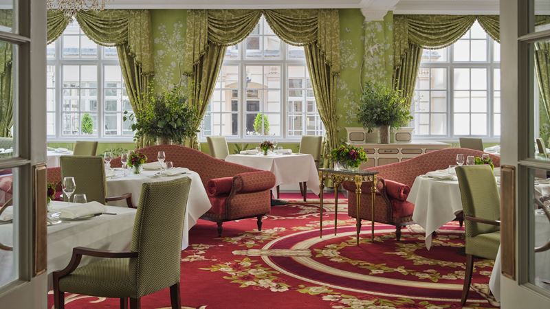 Step inside The Dining Room at The Goring for a romantic meal in elegant surroundings. Credit: The Goring. Image courtesy of The Goring. The elegant interiors of The Dining Room at The Goring, featuring pastel green curtains and chairs, red banquettes and carpet, and white tablecloths.