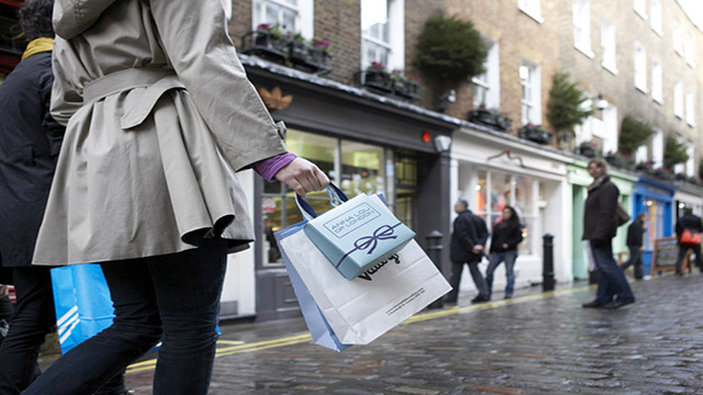 Séance shopping à Londres Newburgh Street, © Newburgh Street Une femme portant un trench coat se balade sur Newburgh Street à Londres avec quelques sacs après une après midi shopping.