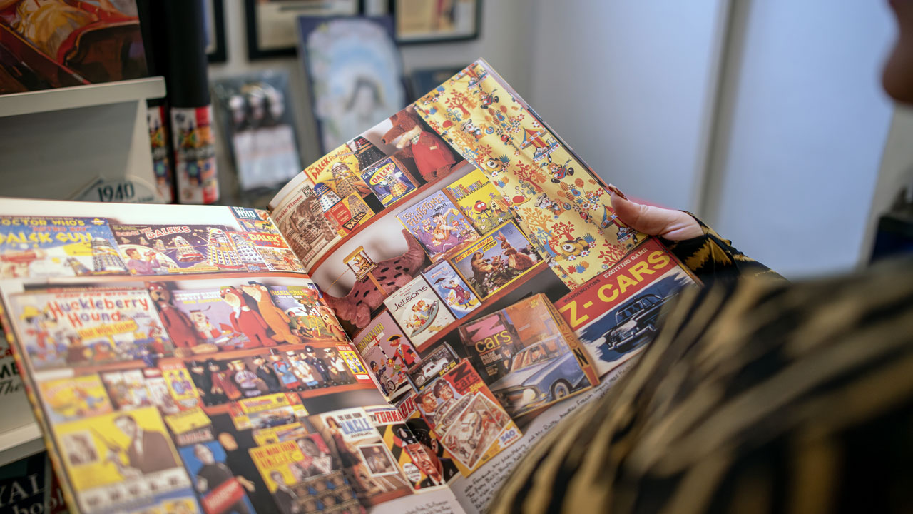 Découvrez ce a quoi ressemblait les pubs dans les journaux et magasines il y a plusieurs décennies en explorant le Museum of Brands. ©London & Partners/Michael Barrow Une personne feuillette un magasine au Museum of Brands, montrant diverses pubs assez colorées datant de quelques décennies.