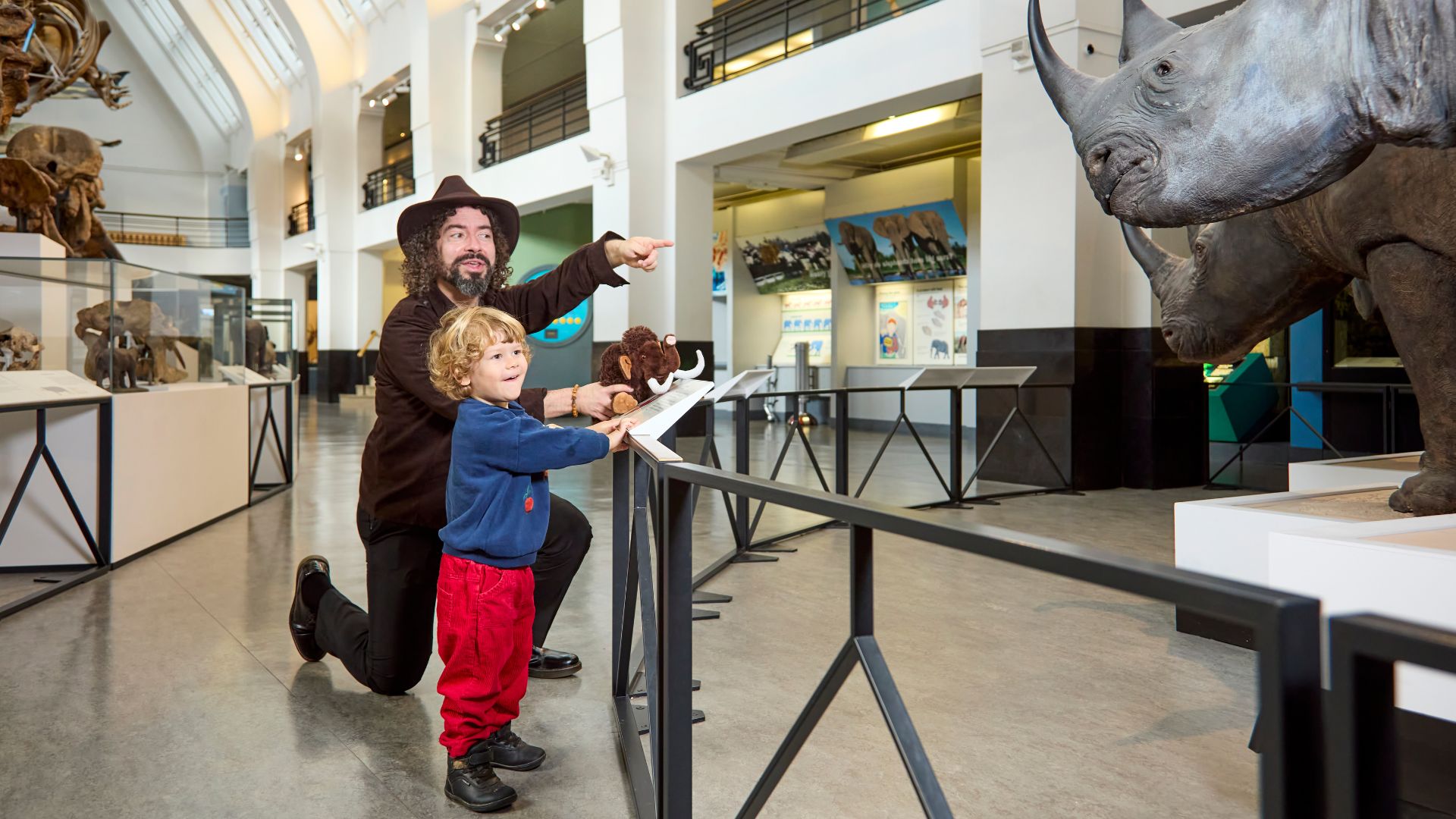 Little ones can learn all about their favourite animals at the Natural History Museum. © Trustees of the Natural History Museum. A young boy and a man in a hat stand pointing at a grey rhino at the natural history museum in London