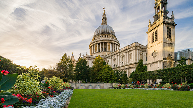 St Paul's Cathedral © visitlondon.com/Jon Reid. Bild mit Genehmigung von visitlondon.com/Jon Reid. Die St. Paul's Cathedral an einem heiteren Tag, mit leichten Wolken am Himmel und einem grünen Rasen und bunten Blumenbeeten im Vordergrund.