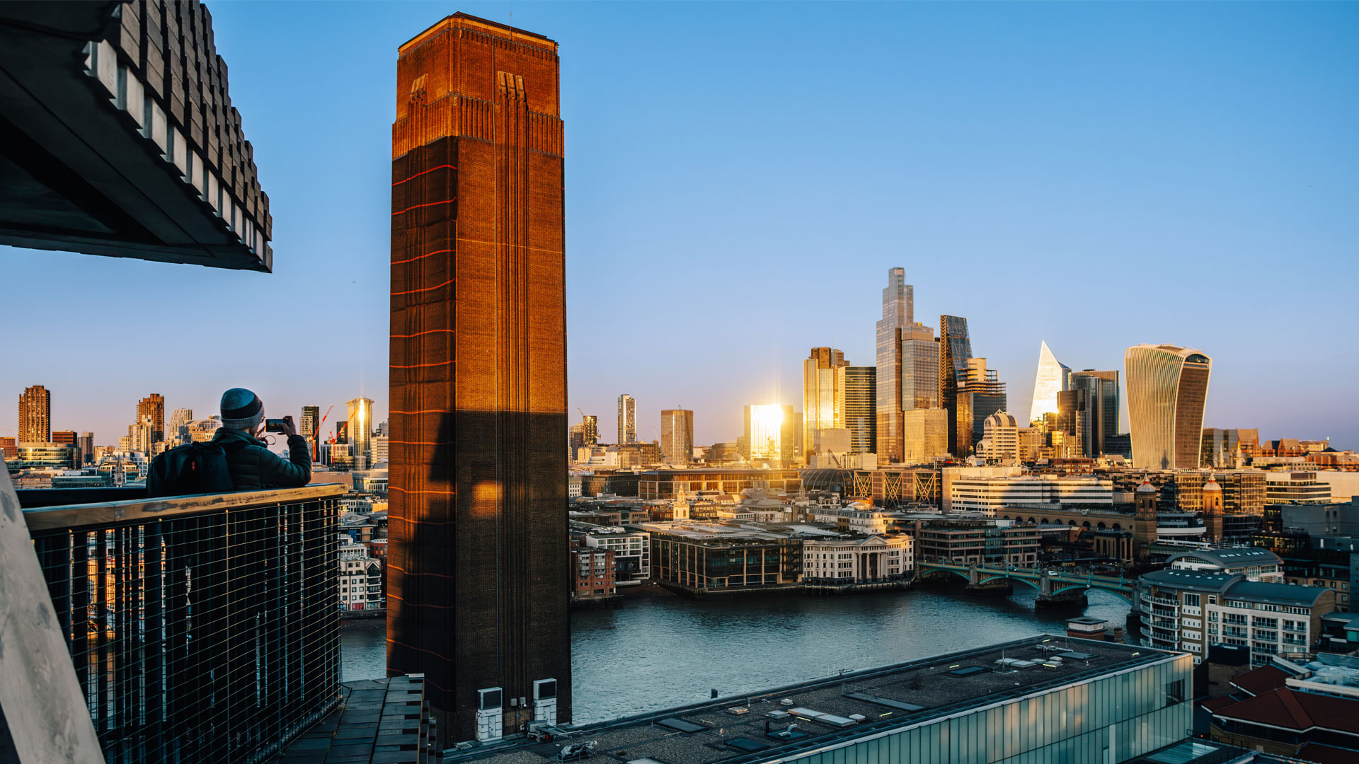Tate Modern viewing terrace. Image credit: London & Partners/ Michael Barrow. Person standing on the Tate Modern viewing terrace taking a picture of the landmarks in the distance.