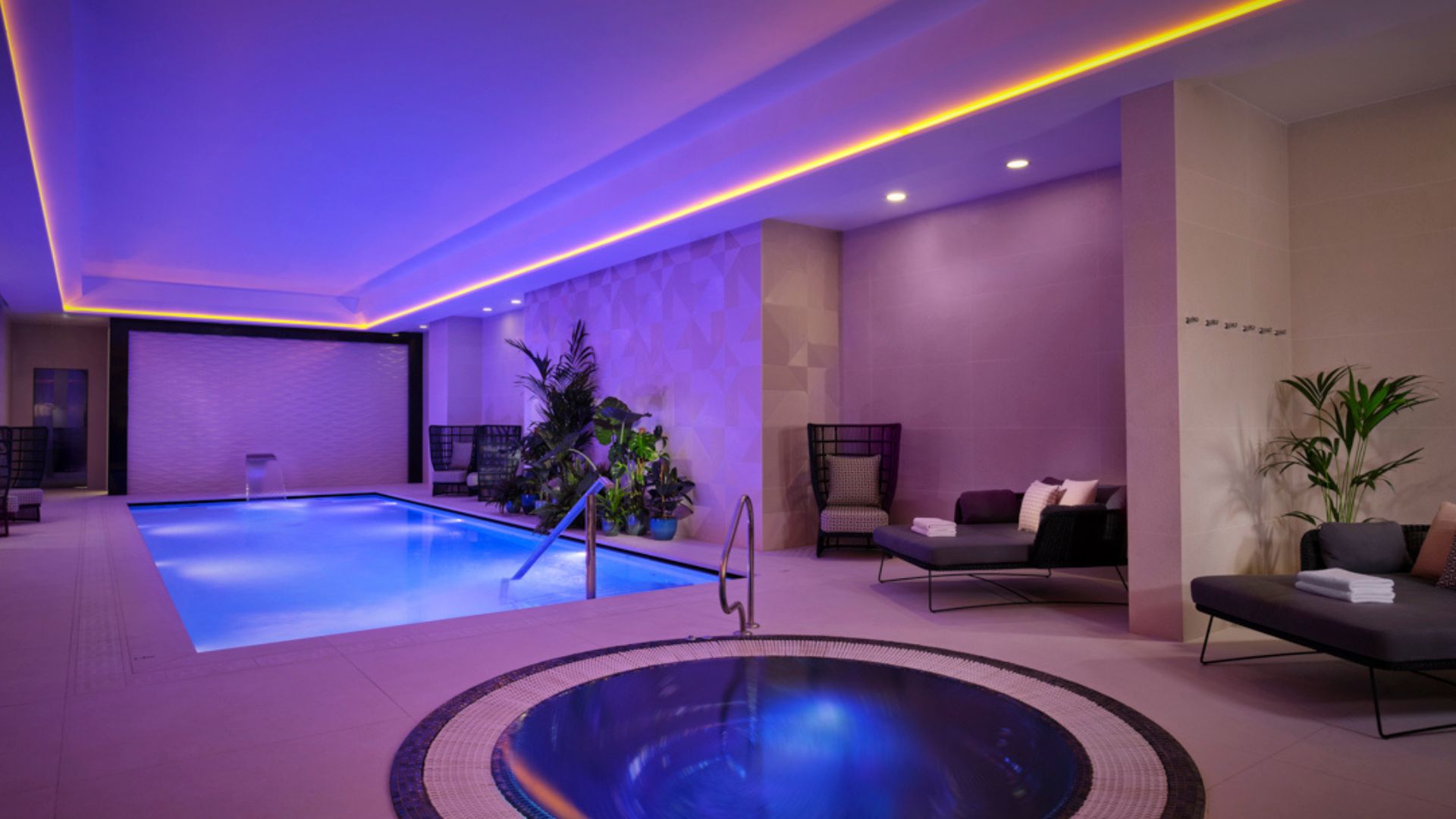BOKEH von Montcalm East. Bild mit Genehmigung von Red Letter Days. Spa-Raum mit violetter und blauer Stimmungsbeleuchtung, einem kleinen runden Whirlpool und einem Pool, mit Sofas an der Seite des Raums.