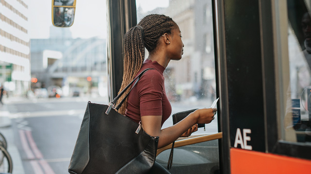Reisen mit dem Bus in London. Bild mit Genehmigung von Shutterstock. Junge schwarze Frau die einen Londoner Bus betritt.