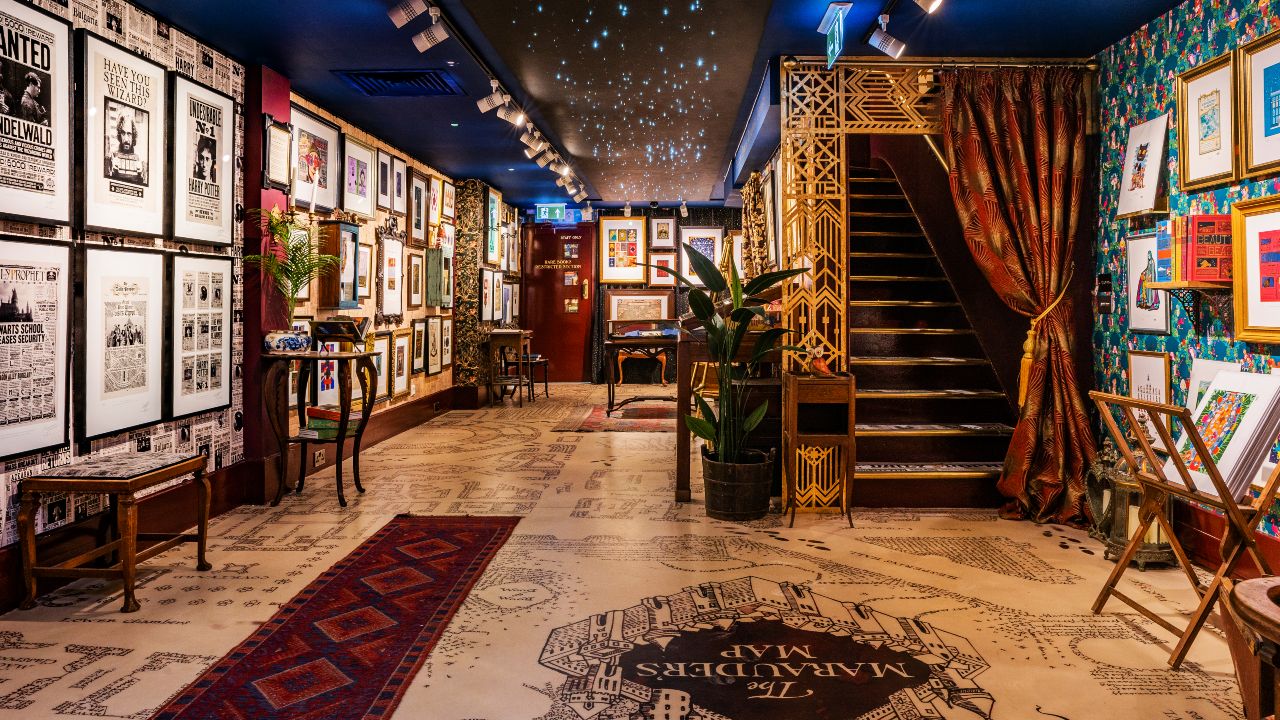 Explore walls covered in prints and graphics. Image courtesy of the House of MinaLima. Inside the colourful House of MinaLima with its walls covered in prints and graphics, a staircase and curtain.