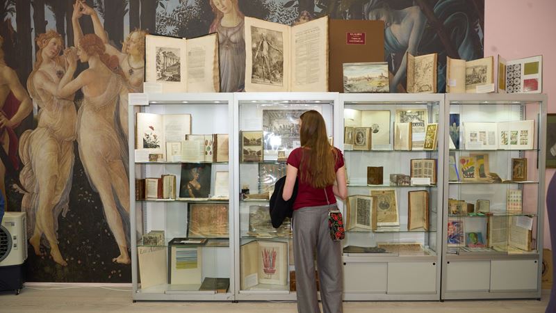 Discover rare first editions, maps and manuscripts at Firsts: London’s Rare Book Fair. Credit: Jon Baker. Image courtesy of Firsts: London’s Rare Book Fair. A person studies books and manuscripts in a display case at Firsts: London’s Rare Book Fair.
