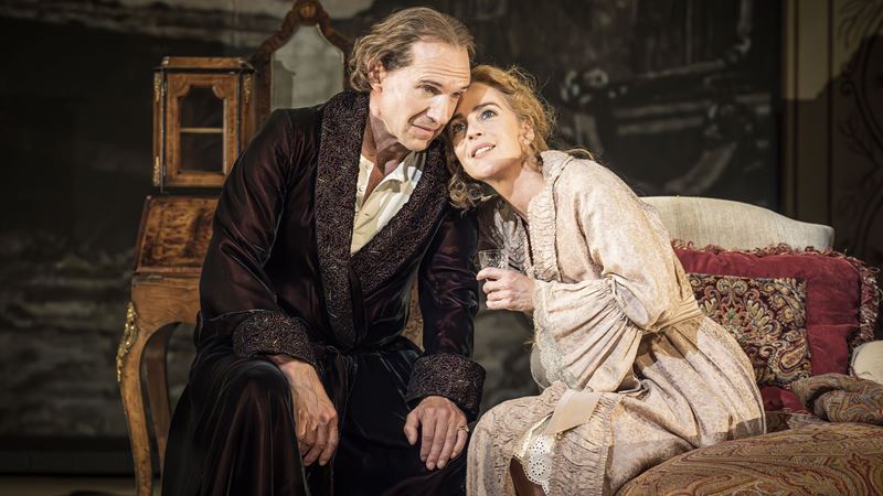 Ralph Fiennes dressed of a velvet dark robe is seating next to Miranda Raison wearing a draped beige gown during a scene of the play Grace Pervades. Ralph Fiennes dressed of a velvet dark robe is seating next to Miranda Raison wearing a draped beige gown during a scene of the play Grace Pervades.