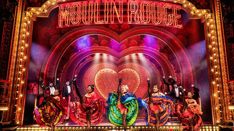 Rediscover the iconic Moulin Rouge on the London stage with plenty of French can-can. Credit: Matt Crockett. Image courtesy of Dewynters. A troup of dancers wearing colourful dresses are dancing the French Cancan on the stage of Moulin Rouge The Musical in London.