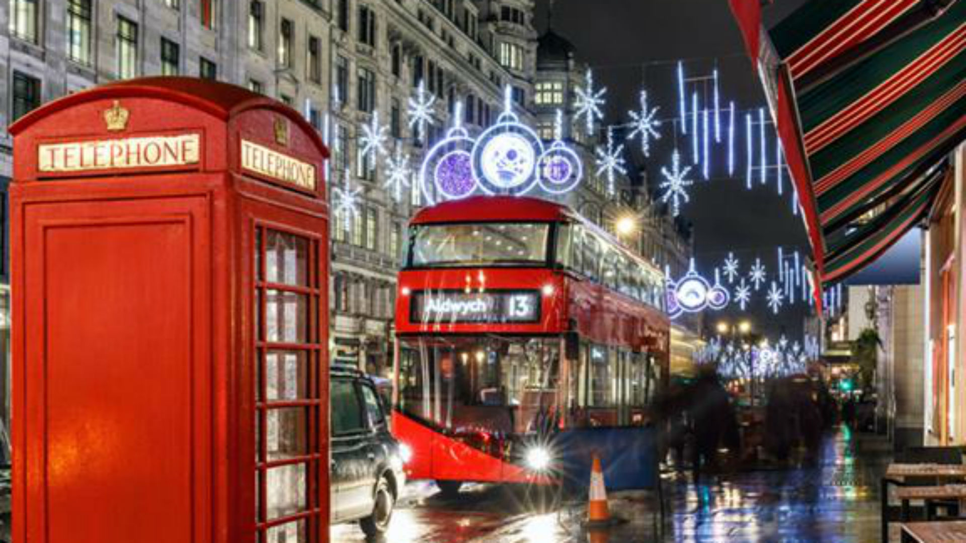 Picture of a traditional red telephone box, red double decker bus with Christmas lights and decorations in the background.