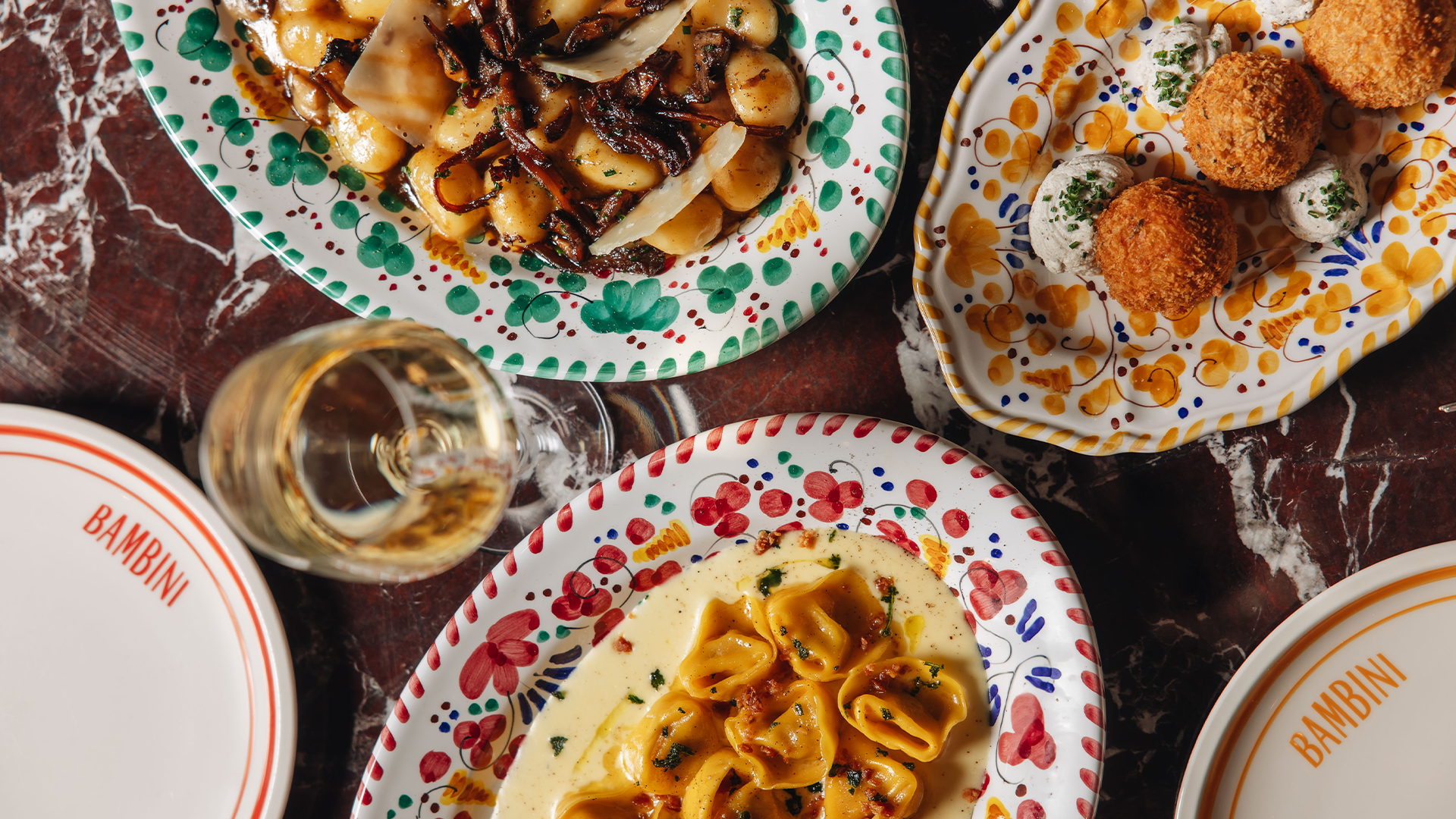 An assortment of pasta dishes, arancini and a glass of white wine