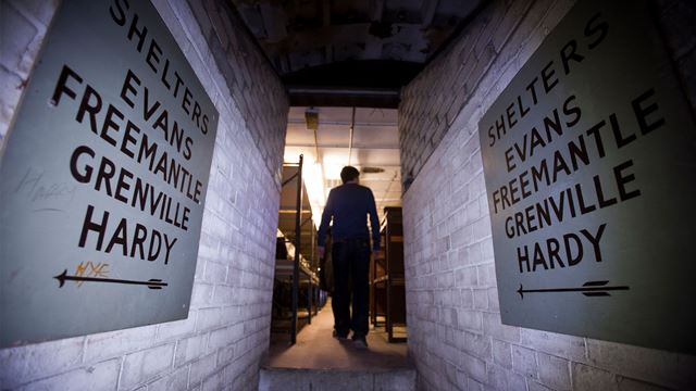 Person walking through small passageway with underground shelter signs and bunkers in distance.