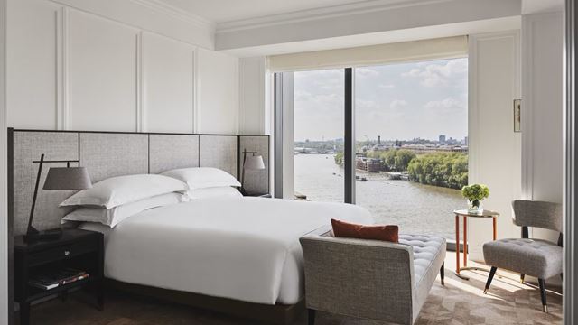 Hotel room with white beddings and huge window overlooking the river Thames and Battersea Park in London on a bright sunny day.
