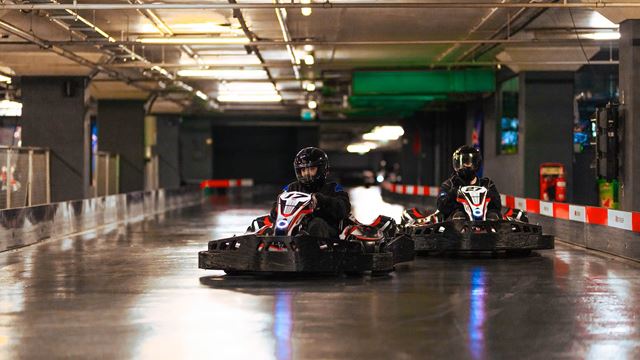 Two racers dressed in black enjoying an indoor go-karting track.