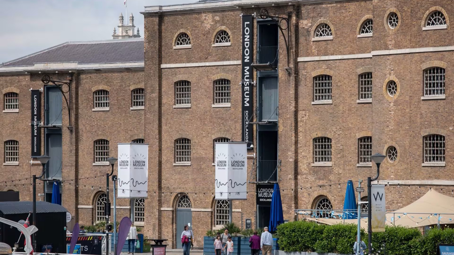 Red-brick facade of the Museum of London Docklands with tourists walking past the entrance.