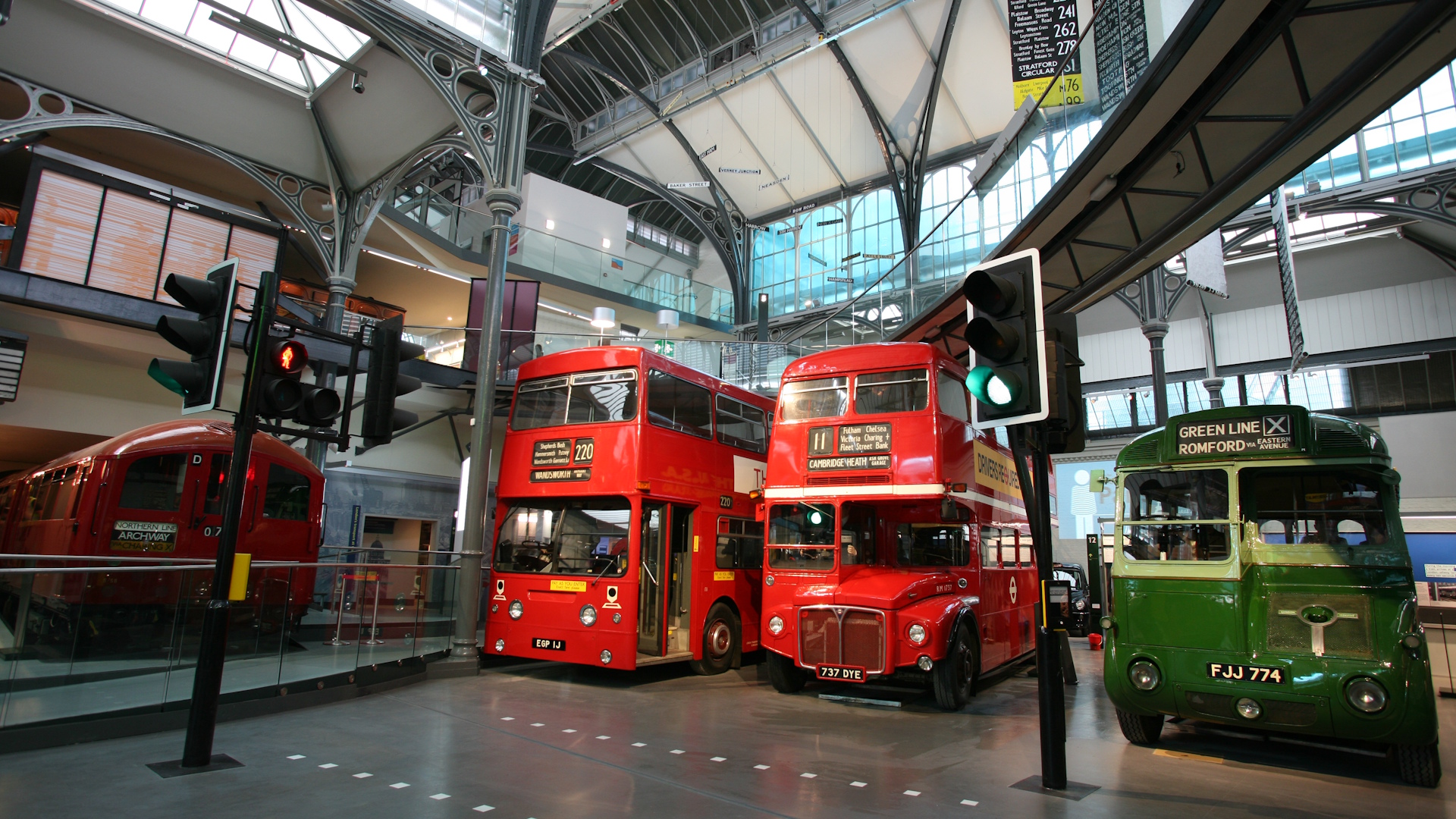Two red double-decker buses and one smaller green bus on display inside the London Transport Museum.