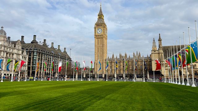 The green space of Parliament Square with flags around each side and Big Ben and the Houses of Parliament in the background