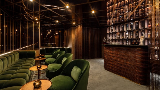 A dimly lit bar area with plush seating, mirrored ceiling and a wall of drinks bottles behind the bar