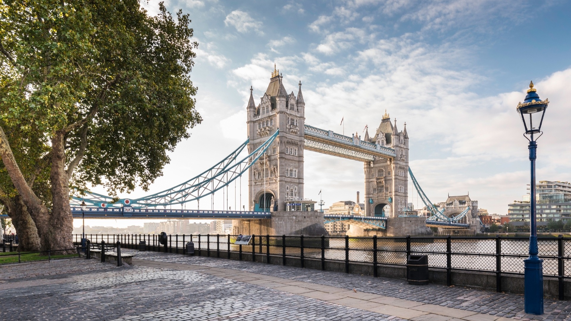 Tower Bridge against a blue sky with little clouds, photographed from the cobbled river path