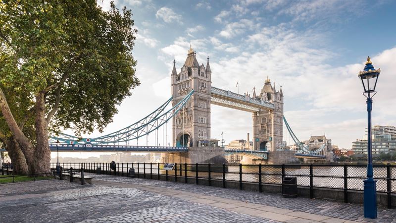 Tower Bridge against a blue sky with little clouds, photographed from the cobbled river path