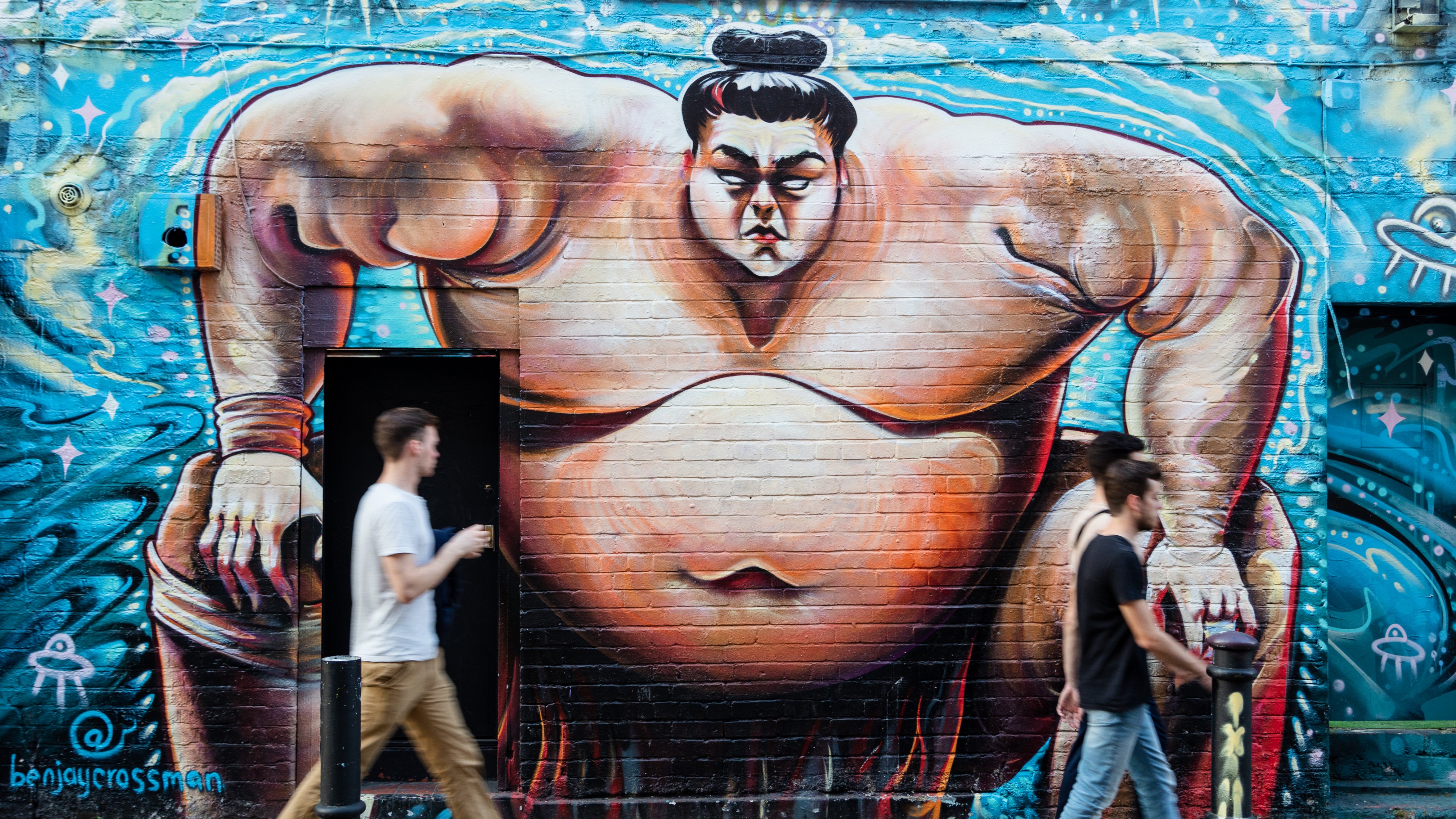 Graffiti in London. Image courtesy of London & Partners/Jon Reid. Graffiti mural of a sumo wrestler against a blue background on a brick wall in Spitalfields
