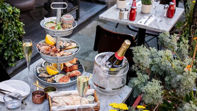 Three-tier seafood platter with oysters, prawns, mussels and crab served with Champagne on an outdoor marble table surrounded by greenery.