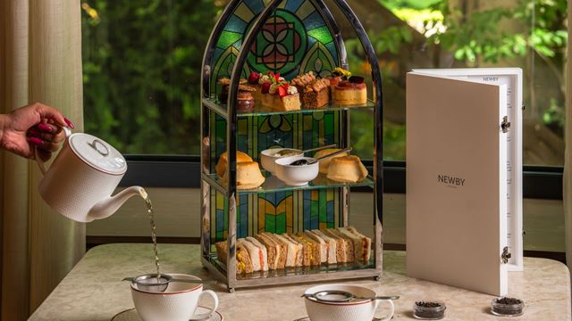 Afternoon tea served on a stained-glass-inspired tiered stand with finger sandwiches, scones and cakes