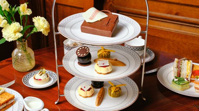 Three-tier afternoon tea stand displaying intricately decorated pastries and cakes alongside sandwiches, served on an elegant wooden table.