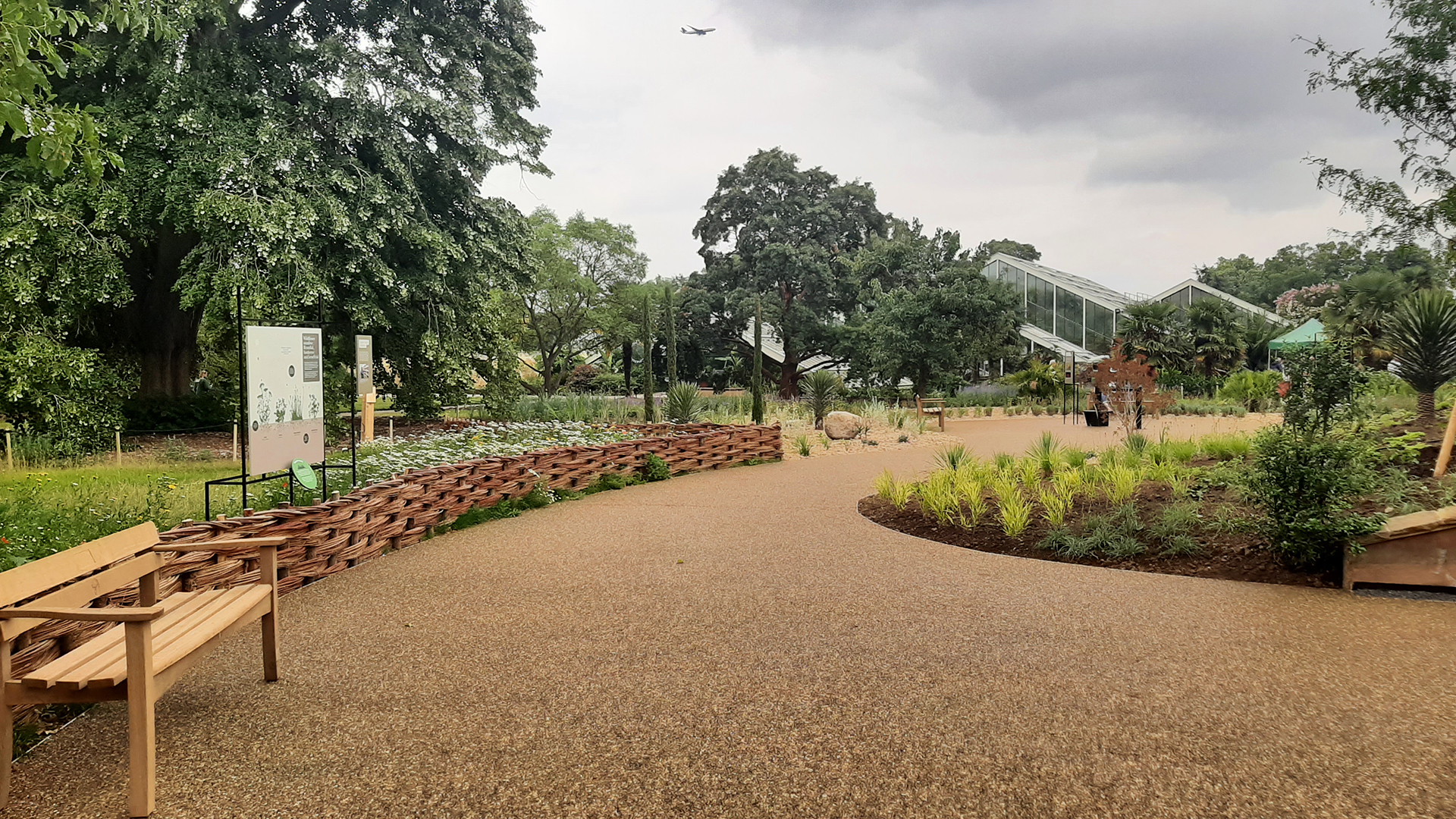 The image shows a curved pavement that is surrounded by plants and flowers with the Princess of Wales conservatory in the background.
