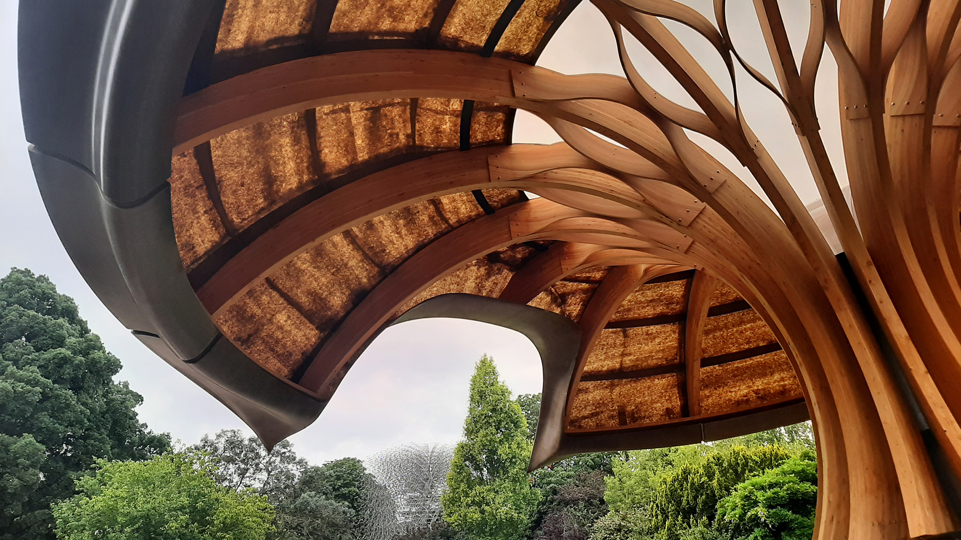 A close up of the pavilion showing wood pannels and other natural materials with trees in the background.