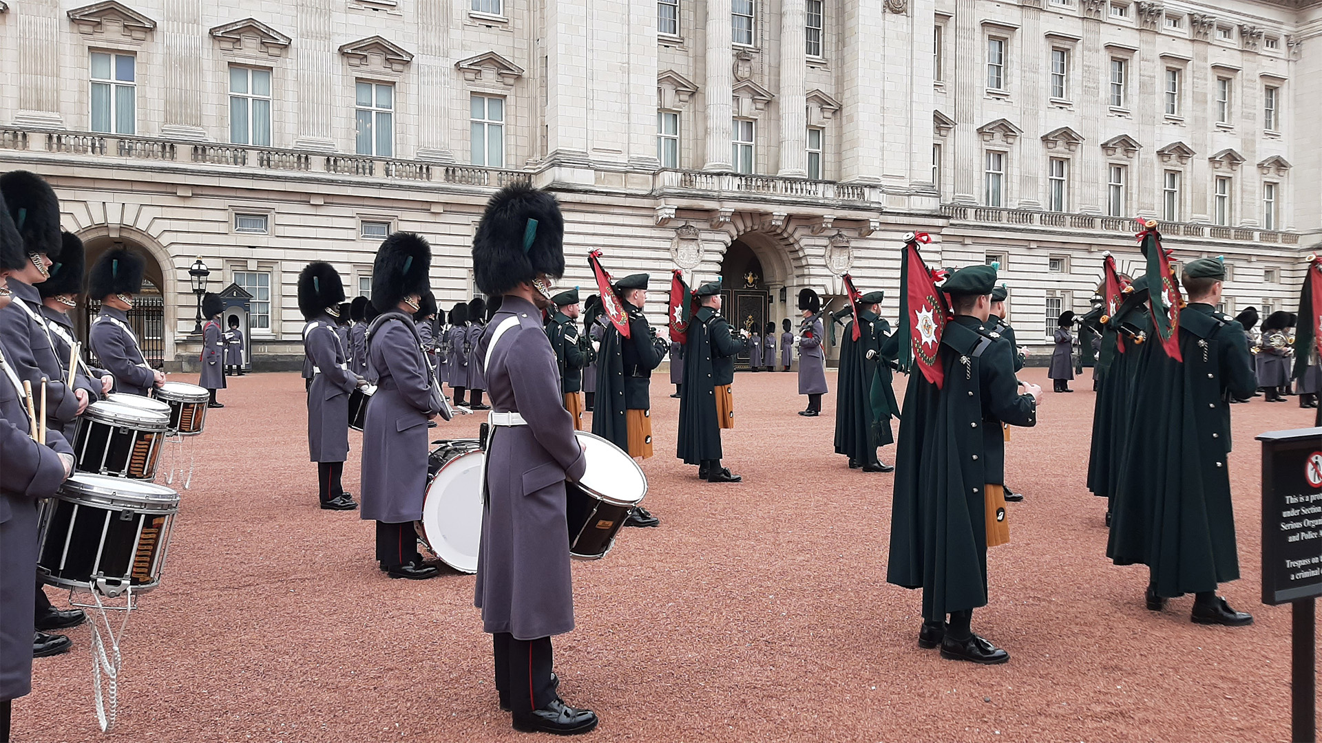 Witness Changing the Guard at the gates of Buckingham Palace. Image courtesy of Visit London/Sigrun Tomicki Sounders with in grey long coats and drums are standing in the courtyard Buckingham Palace drumming and Scottish soldiers stand in front of them with sand colour quilts holding bagpipes