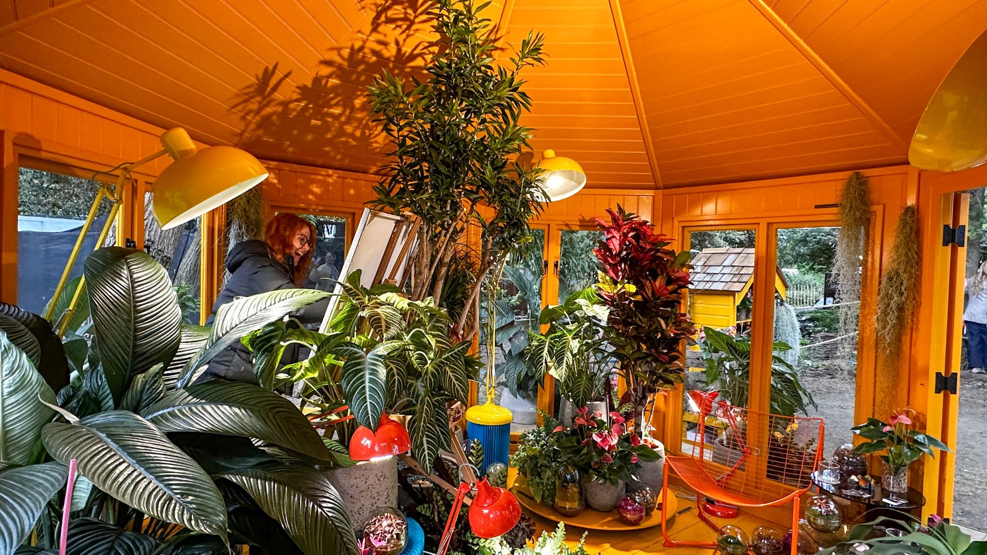 Artist painting inside the Heliotropic Carousel installation surrounded by planting.