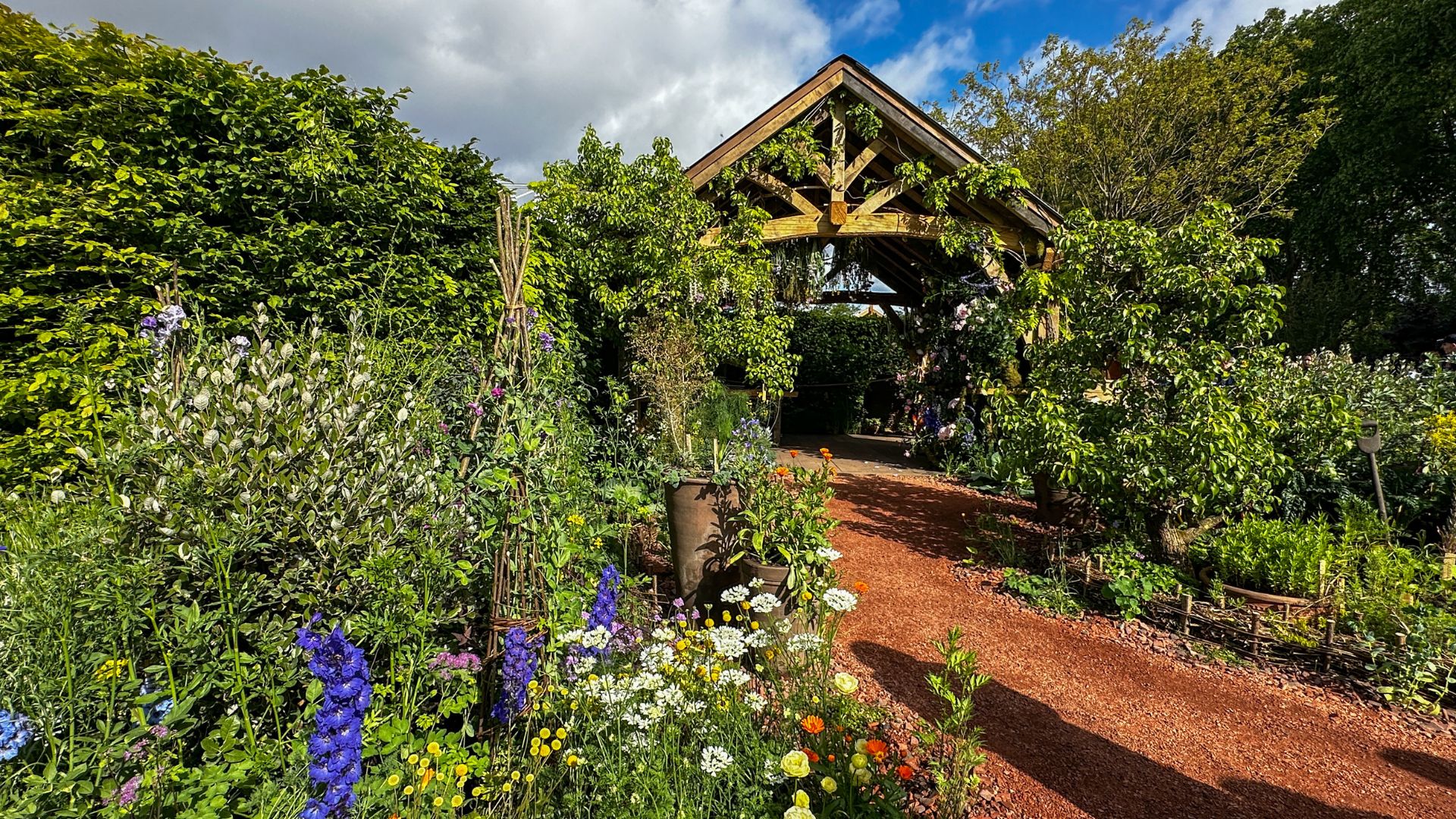 Pathway leading through The King’s Foundation Garden surrounded by flowers and timber structures.