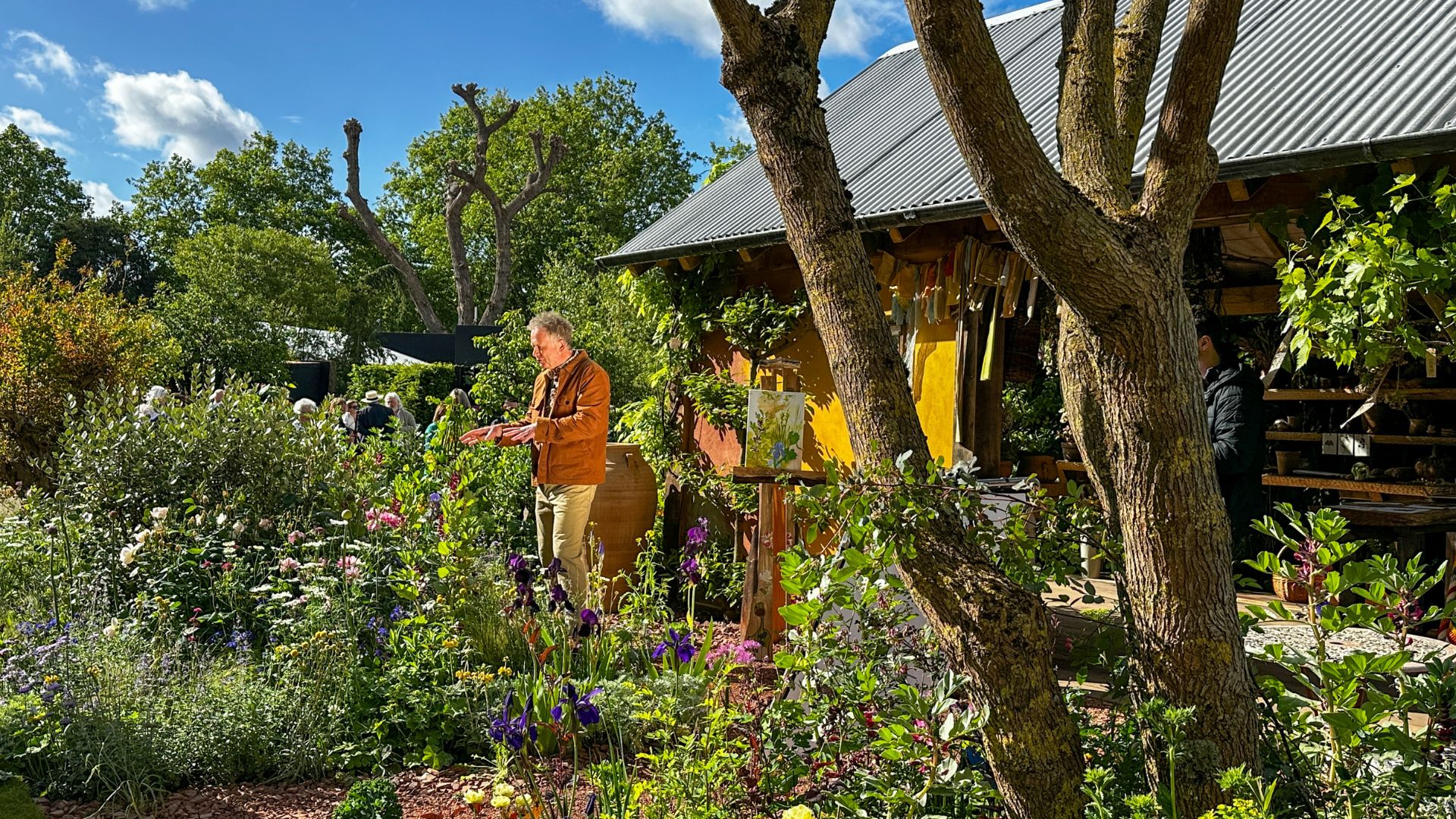 Explore The King’s Foundation Garden, designed to encourage curiosity through diverse planting and traditional craftsmanship. Photo credit: Kirstine Spicer. Man speaking beside the King’s Foundation Curious Garden surrounded by planting.