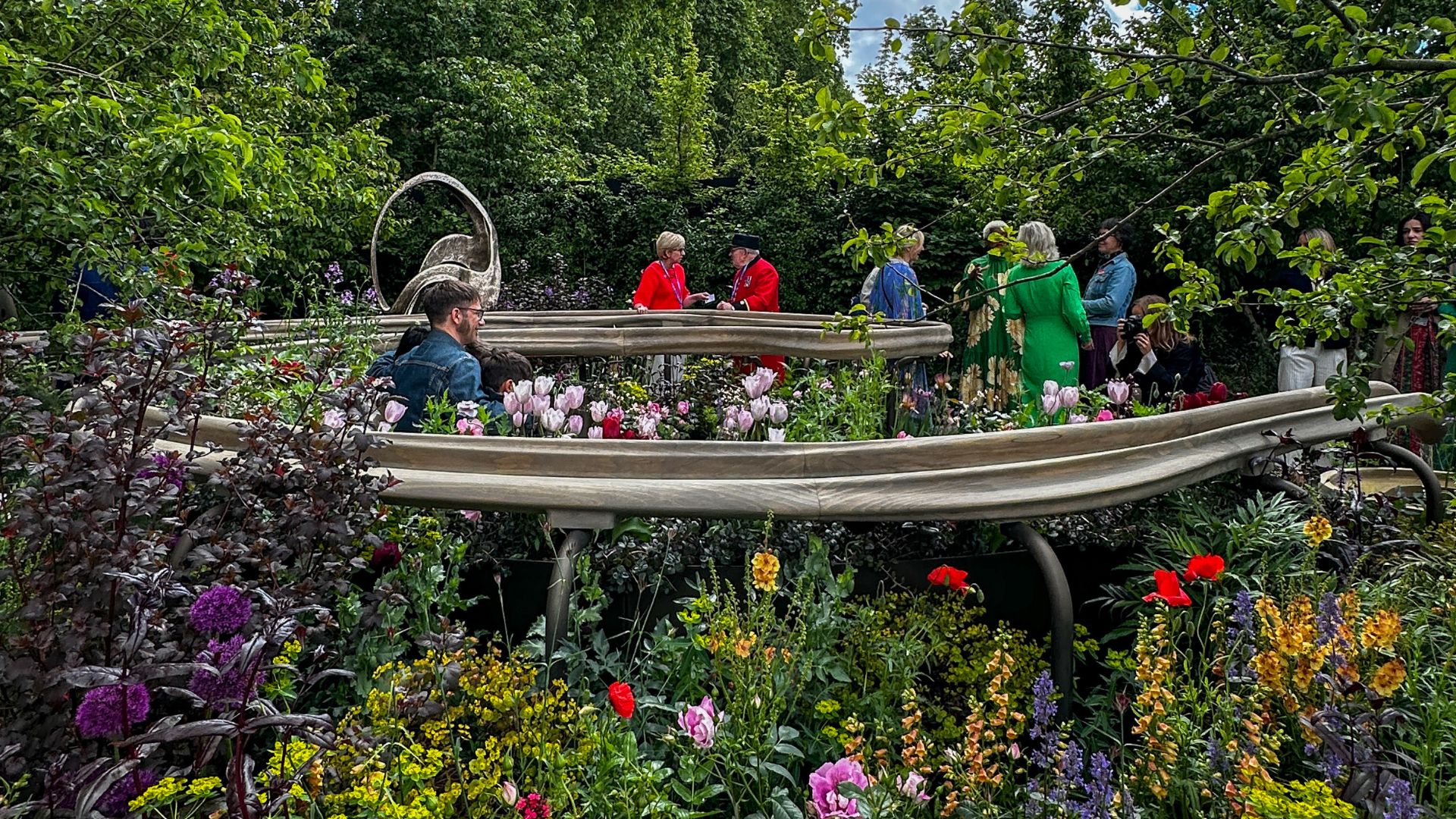 Explore the Parkinson’s UK Garden, where accessible design and thoughtful planting create a calming space to pause. Photo credit: Kirstine Spicer. Visitors standing within the Parkinson’s UK Garden surrounded by planting and curved pathways.