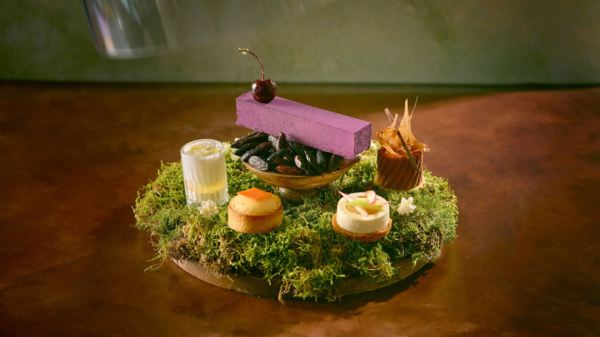 Selection of floral-inspired afternoon tea desserts served on a moss-covered display, including pastries, mousse and a cherry garnish at The Langham.