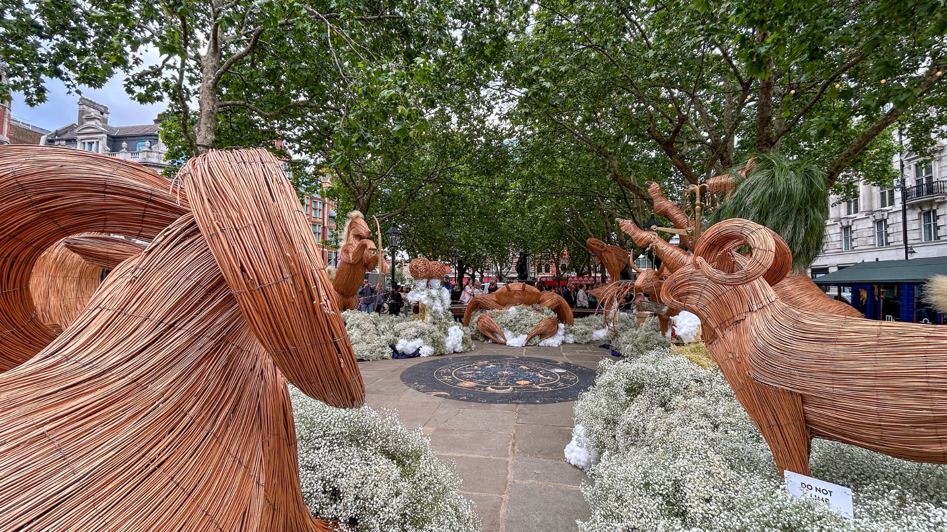 Wicker animal sculptures arranged around a circular plaza with white flowers and trees, part of a Chelsea in Bloom outdoor installation