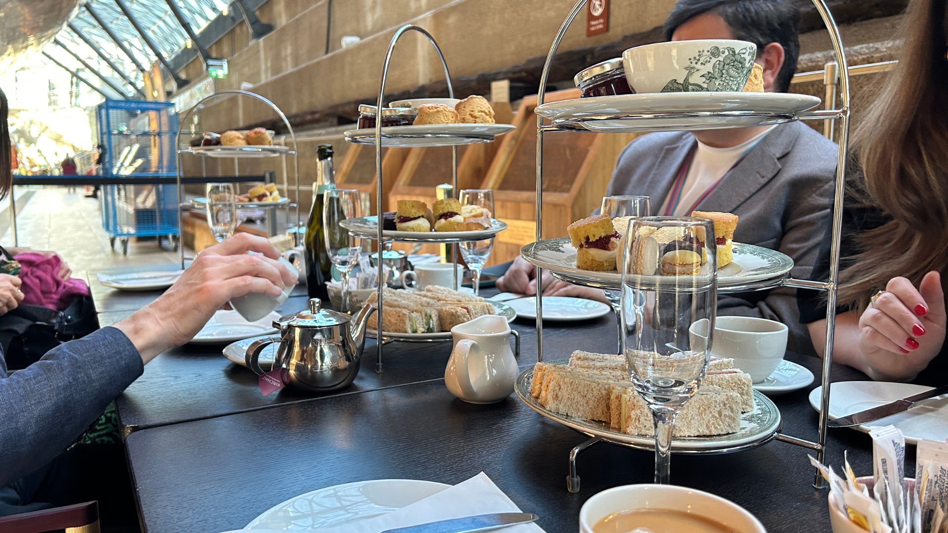 Indulge in a traditional afternoon tea with a historical twist at the Cutty Sark. © Visit London/Hannah Cornish people sat a dark long table with tiered afternoon stands with sweet and savoury treats, and cups of tea and glasses of prosecco on the table