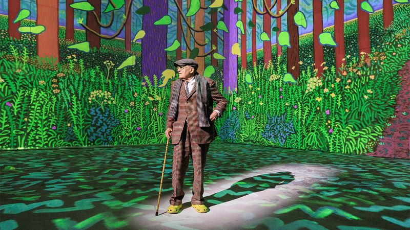 David Hockney against a backdrop of one of his paintings projected at Lightroom.