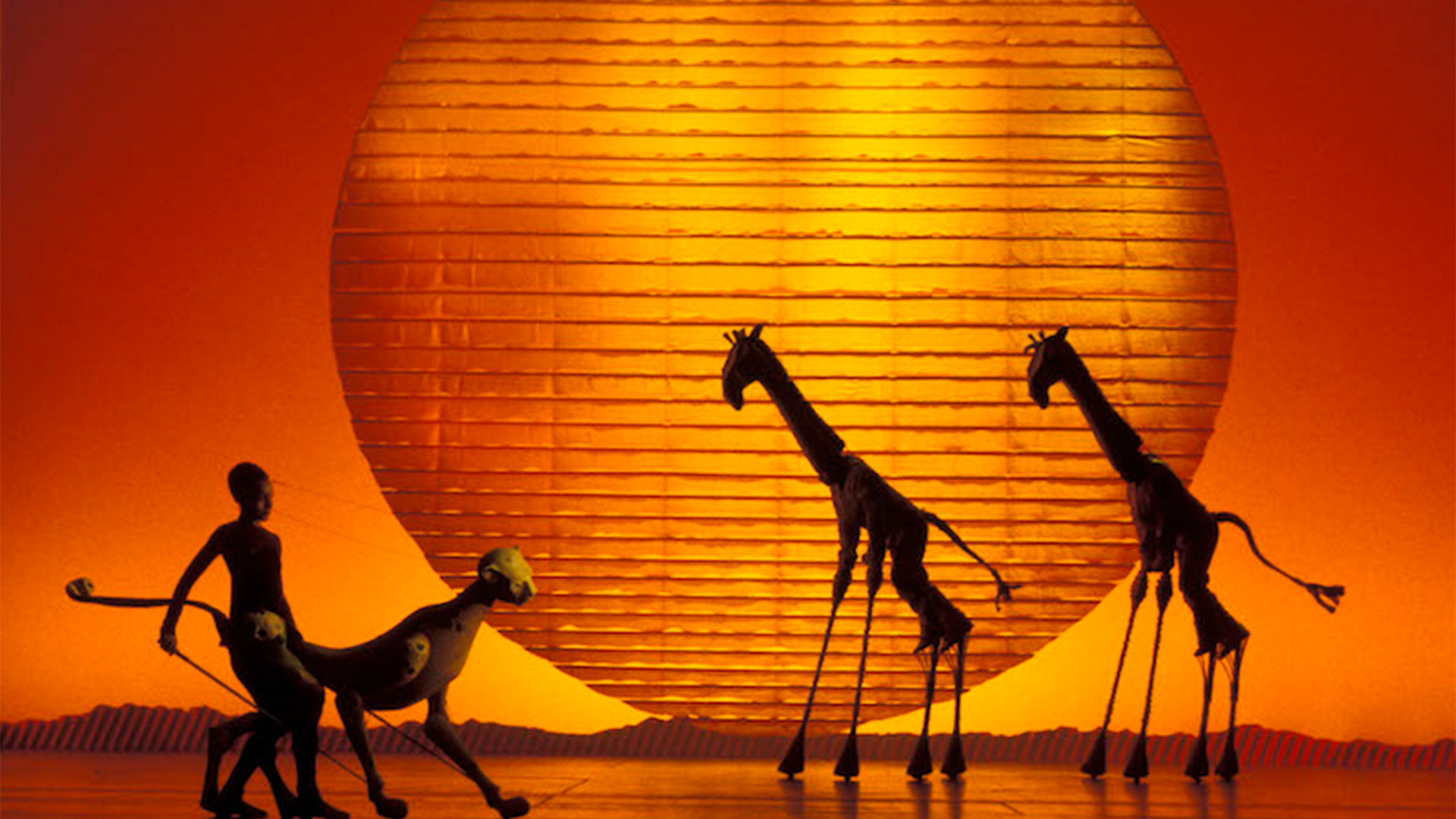 Giraffes and a cheetah glide across the stage in Disney's The Lion King