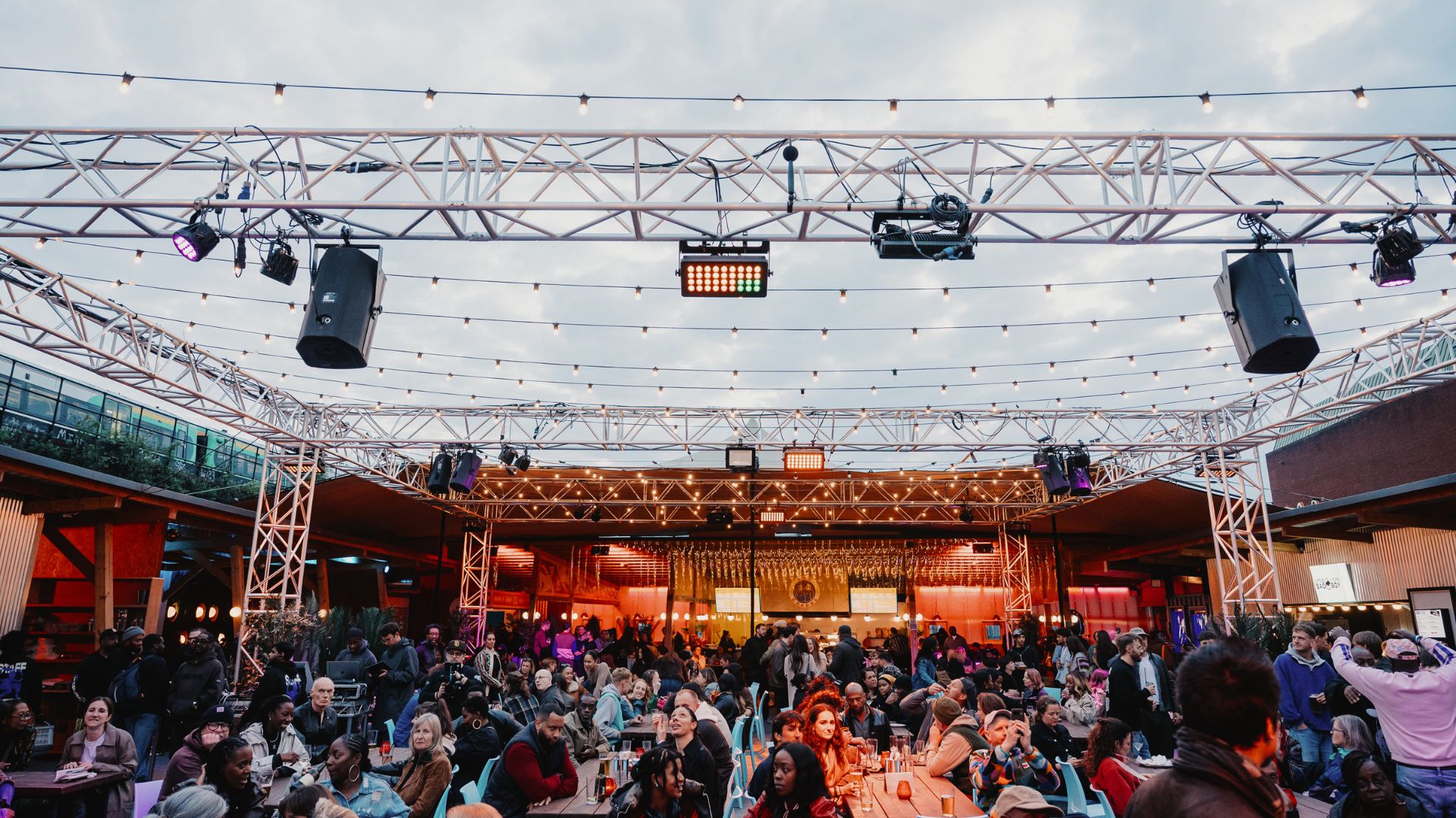 Crowds gather at Freight Brixton's rooftop venue, with food, drinks and live entertainment beneath festoon lighting.