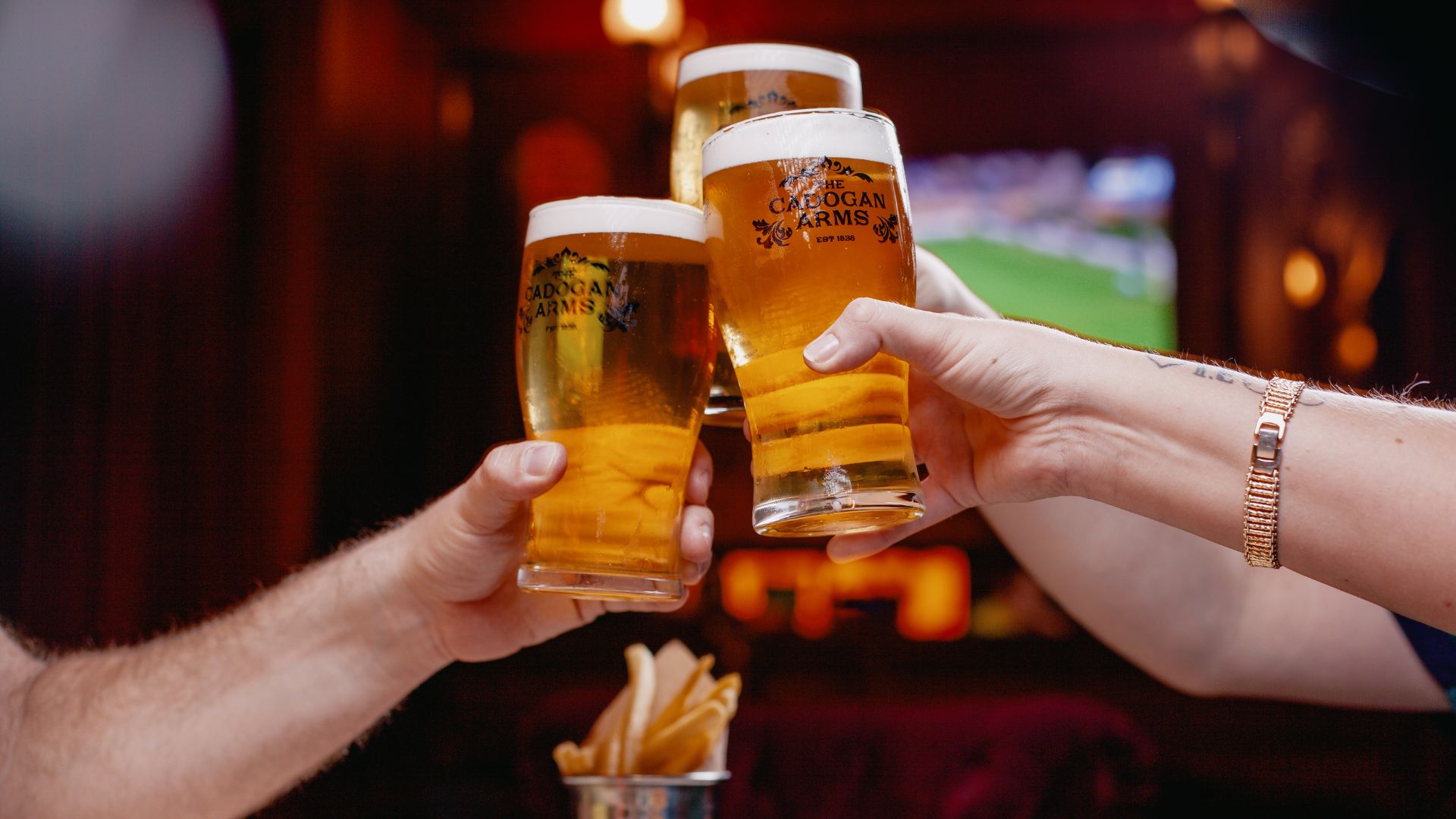 People raise pints while watching football at The Cadogan Arms in Chelsea.