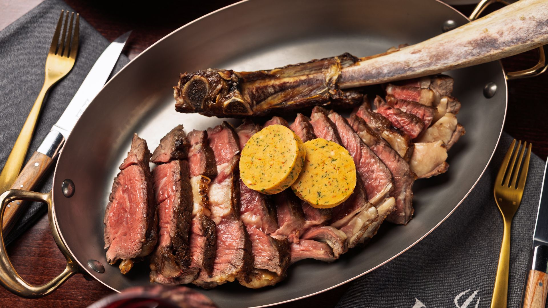 Sliced wagyu tomahawk steak served in a pan with herb butter, showing pink centre and bone.