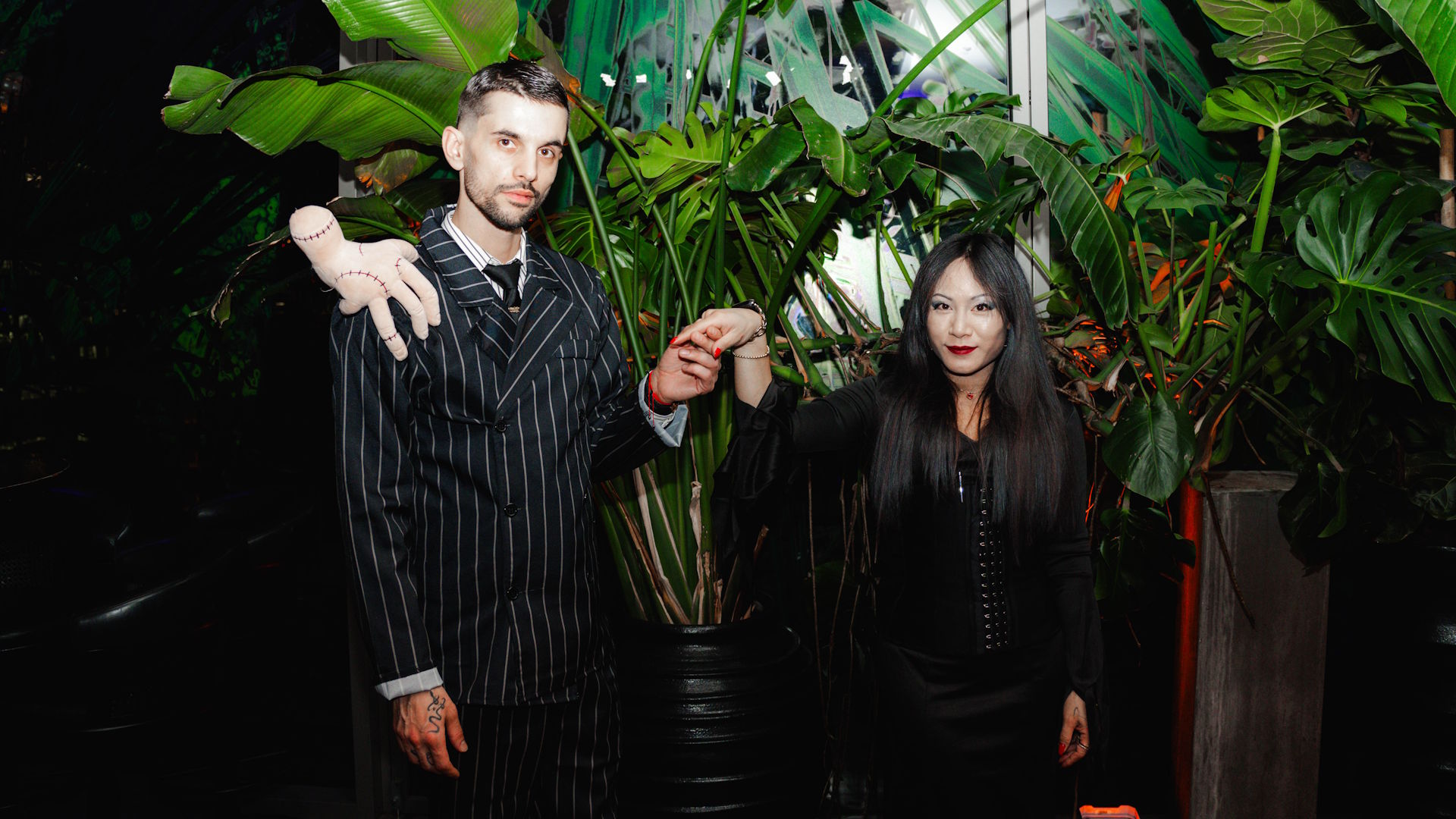 A man and woman wearing Halloween costumes pose in front of tropical plants at 12th Knot, for its Halloween party.