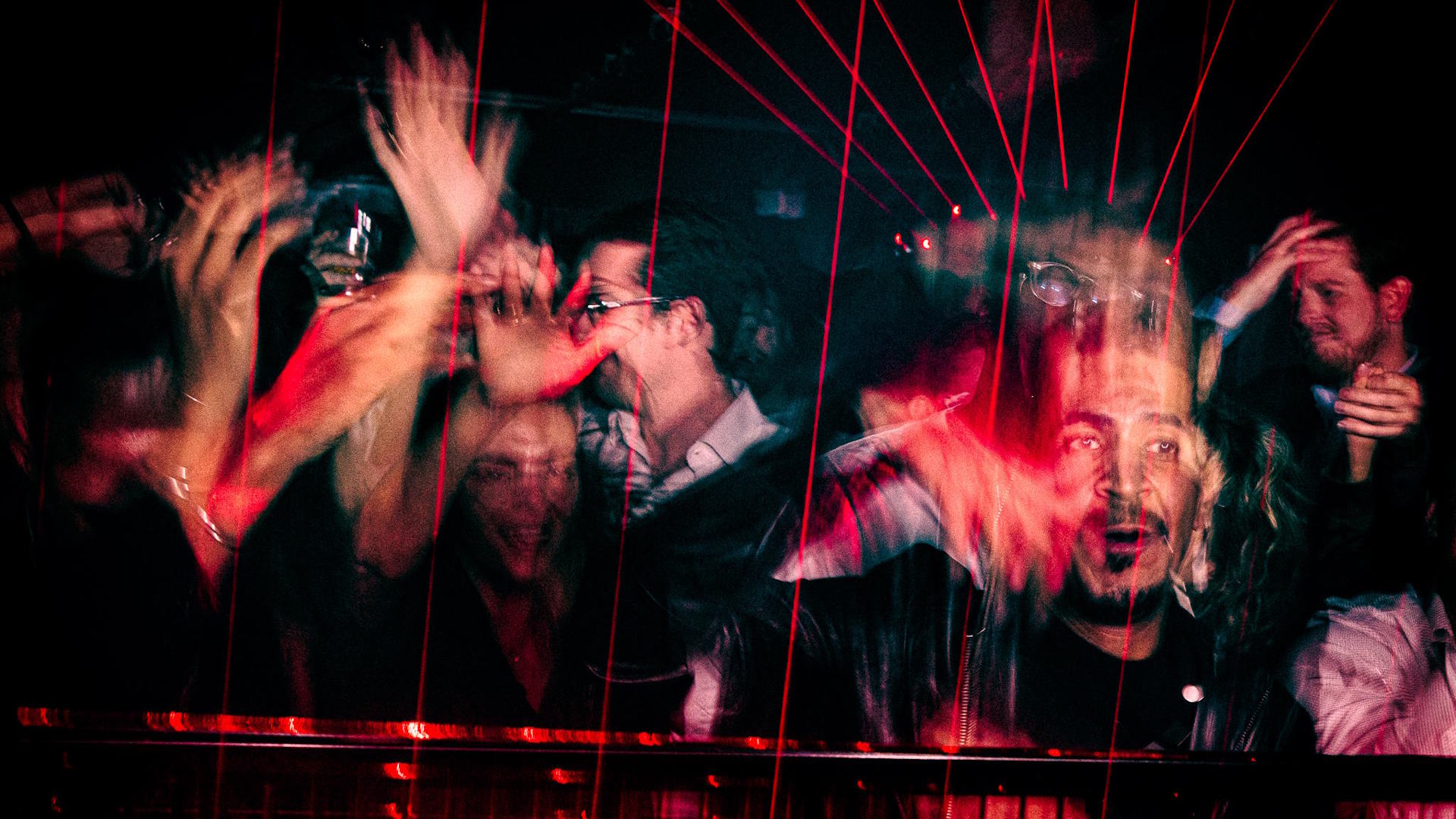 Revellers dance in a dark room with red lasers overhead.