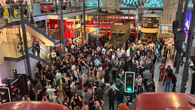 Revellers wearing headphones dance in the hall at the London Transport Museum during a silent disco, surrounded by historic London buses.
